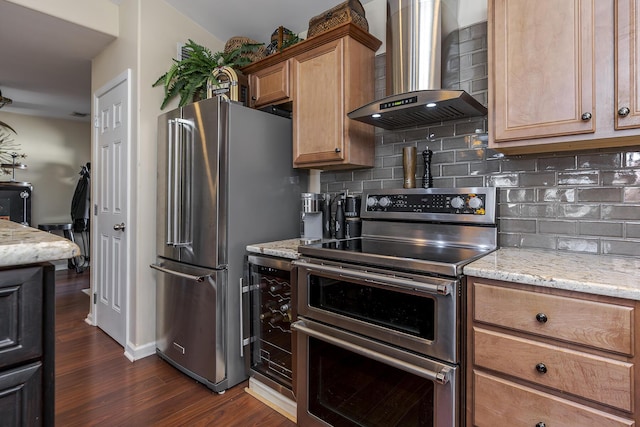 kitchen with light stone countertops, wall chimney range hood, tasteful backsplash, and appliances with stainless steel finishes