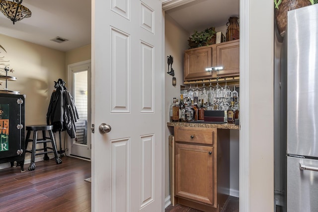 bar with visible vents, decorative backsplash, dark wood-type flooring, freestanding refrigerator, and bar