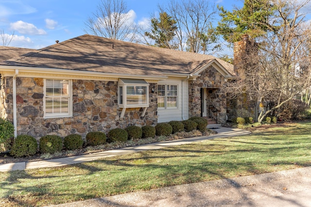 view of front of house with stone siding, a front lawn, roof with shingles, and a chimney