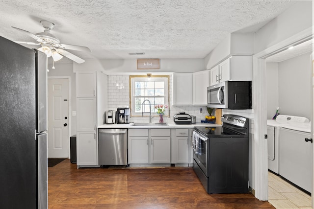 kitchen with separate washer and dryer, a sink, white cabinetry, light countertops, and appliances with stainless steel finishes