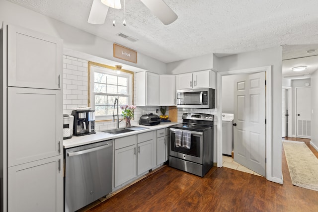 kitchen featuring stainless steel appliances, a sink, visible vents, light countertops, and dark wood-style floors