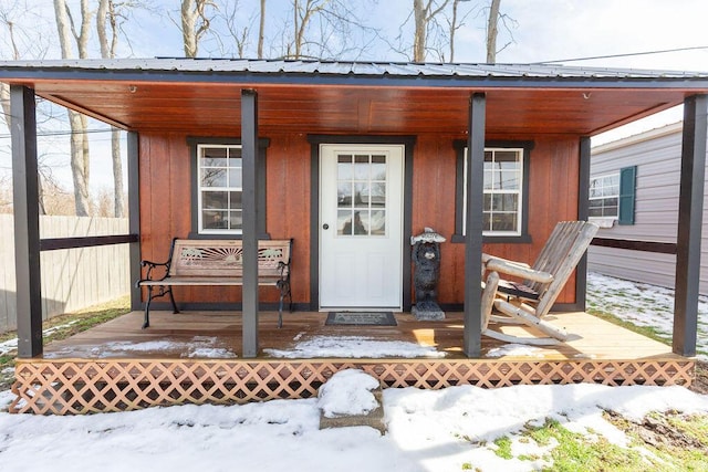 snow covered property entrance with a porch, metal roof, and fence