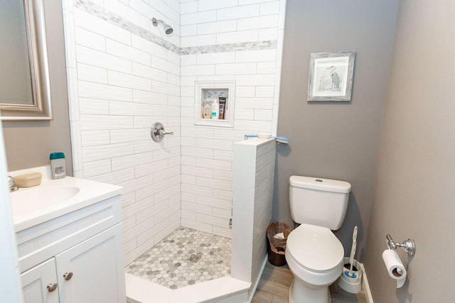 bathroom featuring toilet, a tile shower, and vanity