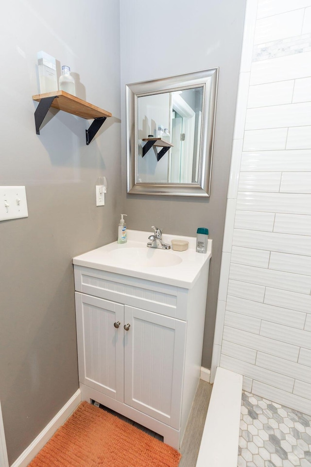 bathroom with baseboards, tiled shower, and vanity