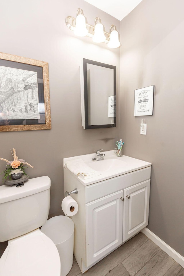 half bath with baseboards, vanity, toilet, and wood finished floors