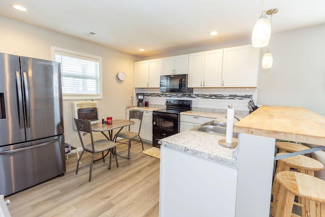 kitchen with light wood-style flooring, decorative light fixtures, light countertops, black appliances, and white cabinetry