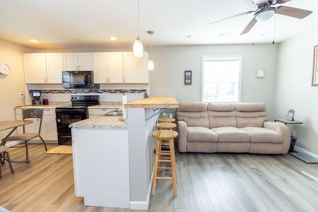 kitchen featuring white cabinetry, open floor plan, black appliances, a kitchen bar, and pendant lighting