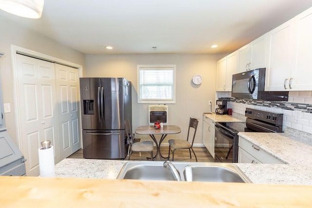 kitchen featuring heating unit, backsplash, white cabinets, a sink, and black appliances