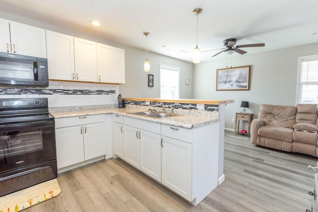 kitchen with a peninsula, a sink, white cabinets, open floor plan, and black appliances