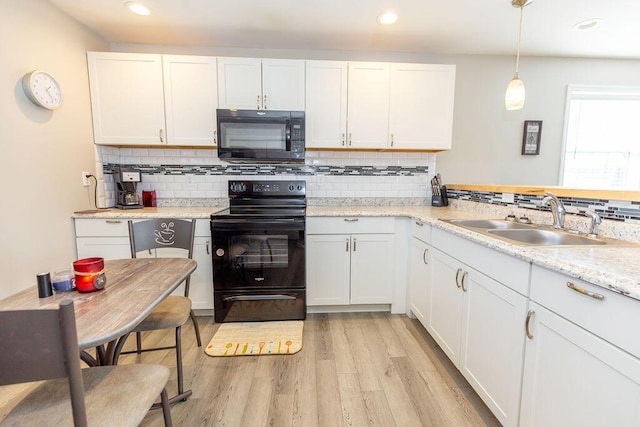 kitchen with a sink, white cabinets, black appliances, light wood finished floors, and pendant lighting