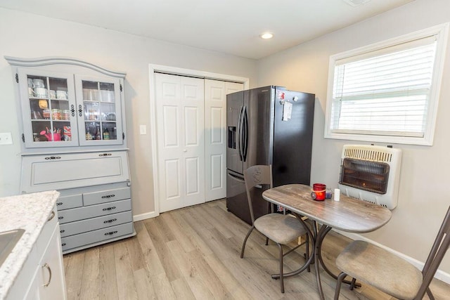 kitchen with heating unit, white cabinetry, light wood-style floors, stainless steel fridge with ice dispenser, and glass insert cabinets