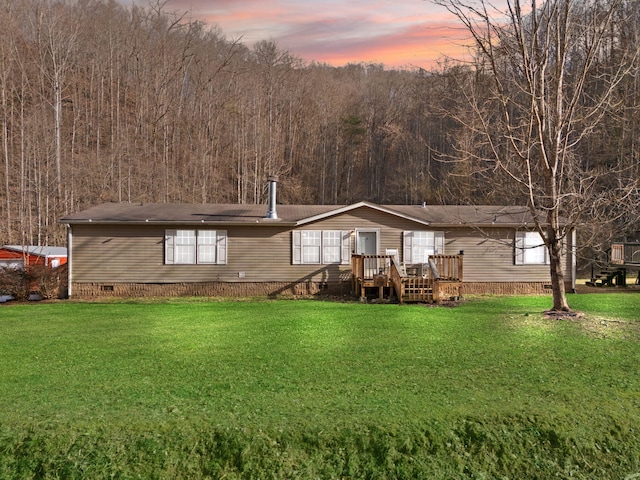 back of property at dusk with crawl space, a lawn, a view of trees, and a wooden deck