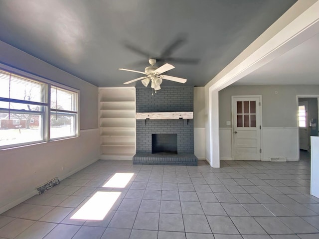 unfurnished living room with ceiling fan, a wealth of natural light, a brick fireplace, and light tile patterned flooring