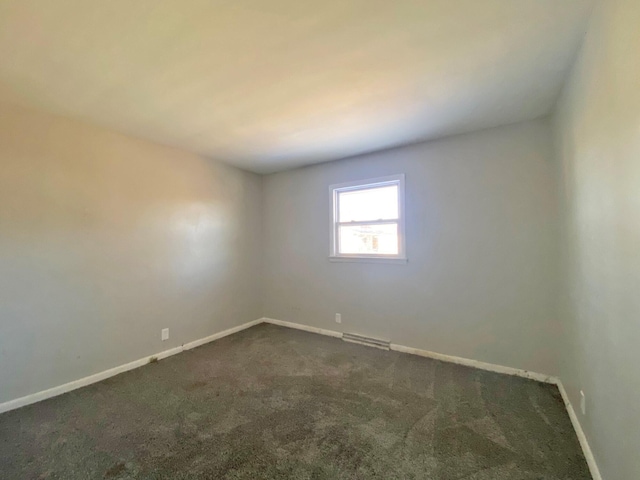 unfurnished room featuring dark colored carpet, visible vents, and baseboards