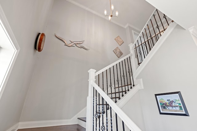 staircase featuring a high ceiling, wood finished floors, baseboards, an inviting chandelier, and crown molding