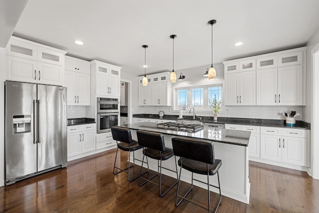 kitchen with a center island, dark wood-style flooring, appliances with stainless steel finishes, white cabinetry, and a kitchen bar