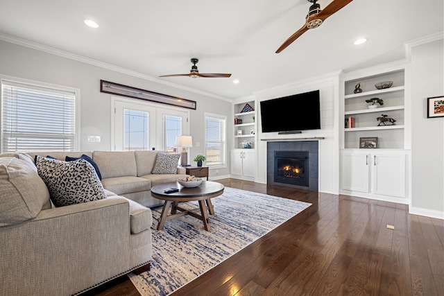 living room with dark wood-style floors, ornamental molding, a ceiling fan, and a tile fireplace