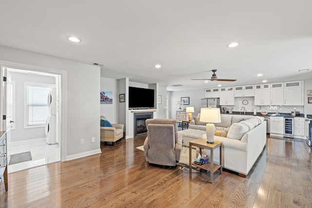 living room with beverage cooler, hardwood / wood-style floors, a glass covered fireplace, and recessed lighting