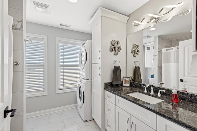 bathroom featuring stacked washer and dryer, marble finish floor, visible vents, and baseboards