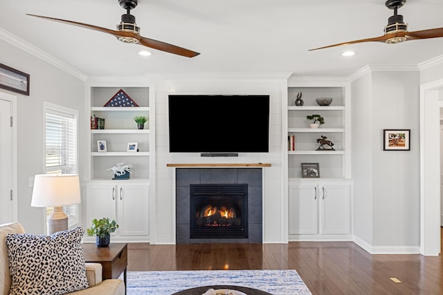 living room featuring a ceiling fan, a tile fireplace, ornamental molding, hardwood / wood-style floors, and built in shelves