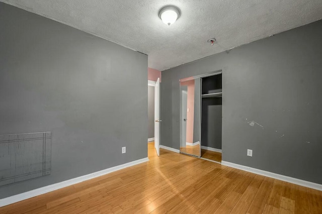 unfurnished bedroom with a closet, a textured ceiling, baseboards, and wood finished floors