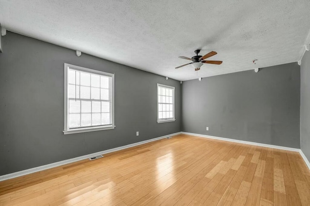 unfurnished room with a textured ceiling, visible vents, a ceiling fan, baseboards, and light wood-type flooring