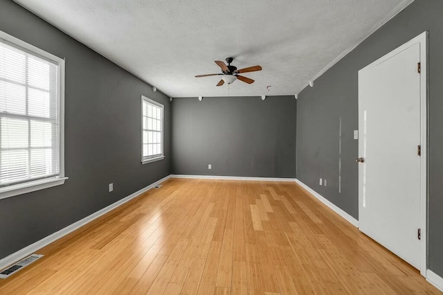 spare room featuring a textured ceiling, a ceiling fan, baseboards, visible vents, and light wood-style floors