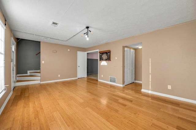 unfurnished room featuring stairs, light wood-style flooring, visible vents, and baseboards