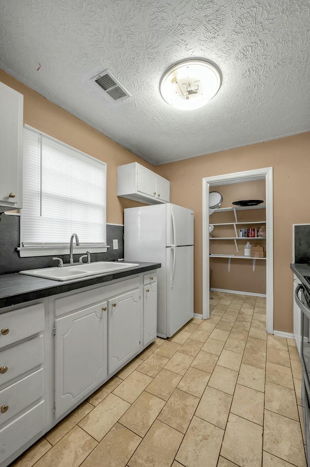 kitchen featuring a sink, visible vents, white cabinets, freestanding refrigerator, and dark countertops