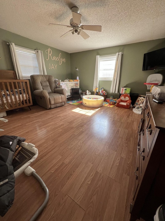 living area with ceiling fan, a textured ceiling, and wood finished floors