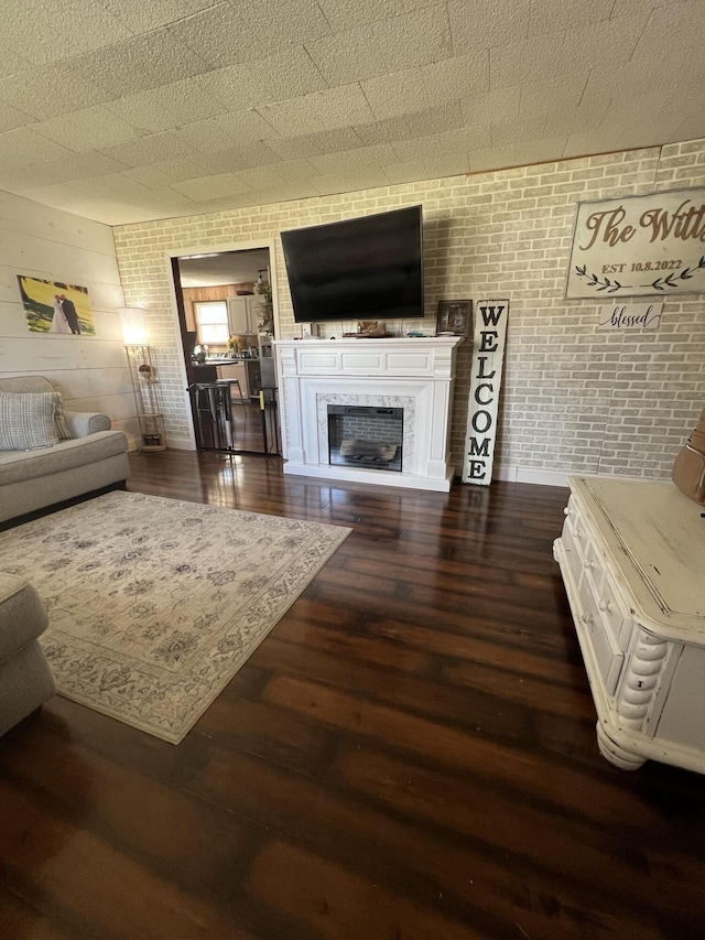 living area with brick wall, dark wood-type flooring, and a high end fireplace