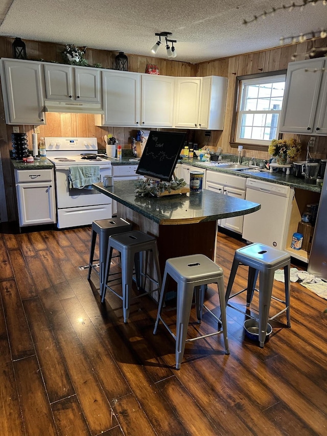 kitchen with white appliances, a kitchen island, dark wood-type flooring, under cabinet range hood, and white cabinetry