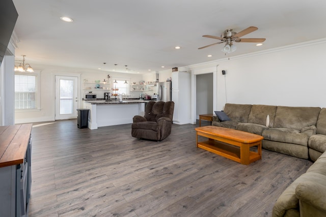 living room with ornamental molding, recessed lighting, dark wood finished floors, and ceiling fan with notable chandelier