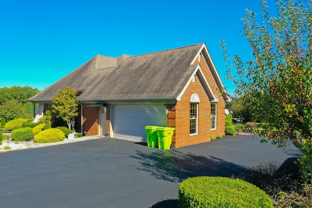 view of front of property featuring a garage, driveway, brick siding, and a shingled roof