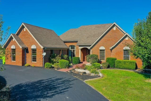 view of front facade with a shingled roof, a front lawn, and brick siding