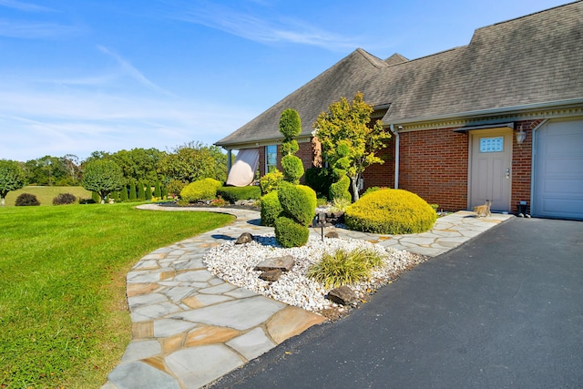 view of front of house with driveway, a garage, brick siding, roof with shingles, and a front yard