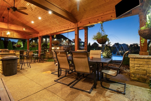 patio terrace at dusk with outdoor dining space, an outdoor bar, and a ceiling fan