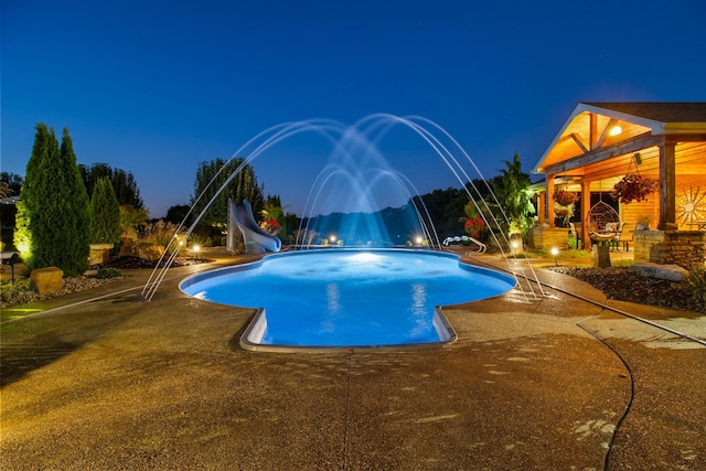 outdoor pool with a water slide and a patio area