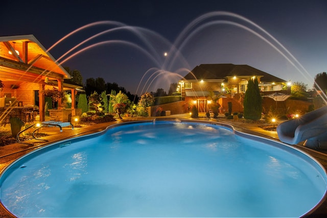 pool at night with an outdoor pool and a water slide