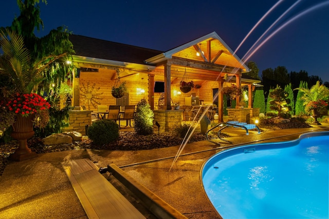 pool at night with a patio area and an outdoor pool