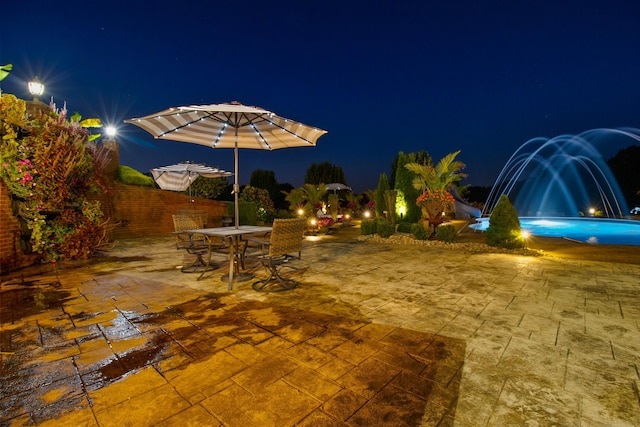 patio at night with a fenced in pool and fence