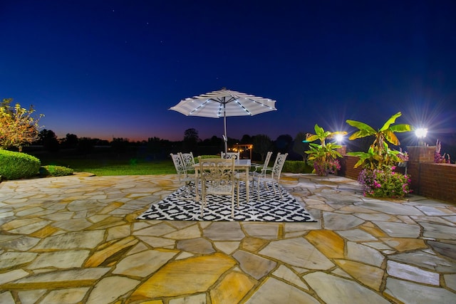 patio at night featuring outdoor dining area and fence