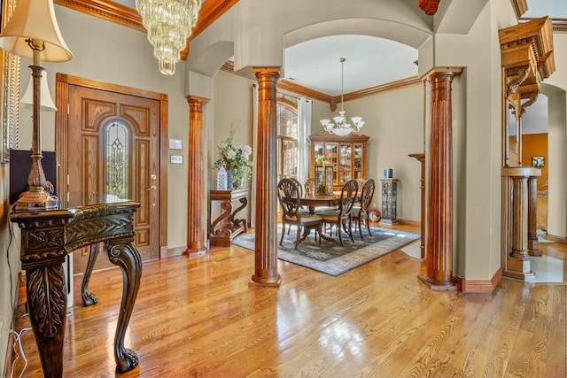 entryway featuring arched walkways, ornamental molding, ornate columns, an inviting chandelier, and light wood-style floors