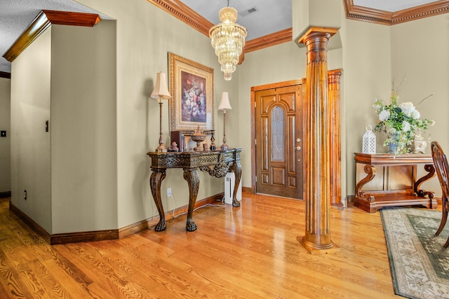 foyer entrance featuring baseboards, light wood-style flooring, ornamental molding, ornate columns, and a notable chandelier