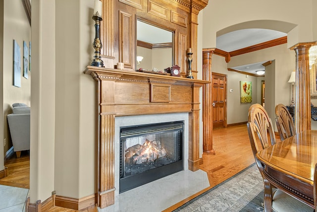 interior space featuring arched walkways, a premium fireplace, baseboards, light wood finished floors, and crown molding