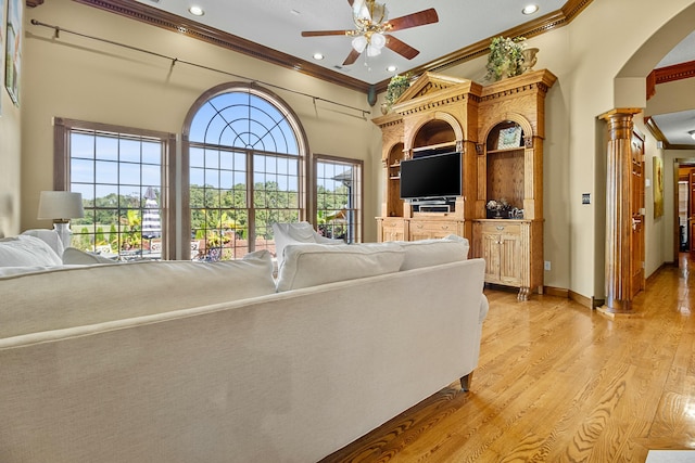 unfurnished living room with decorative columns, a ceiling fan, a towering ceiling, crown molding, and light wood-style floors