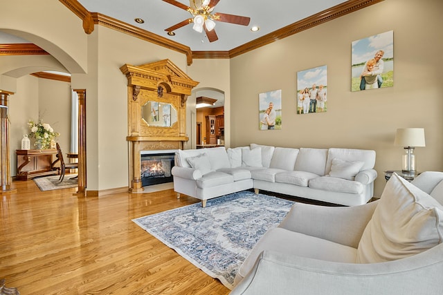 living room featuring arched walkways, ornamental molding, a high end fireplace, ceiling fan, and wood finished floors