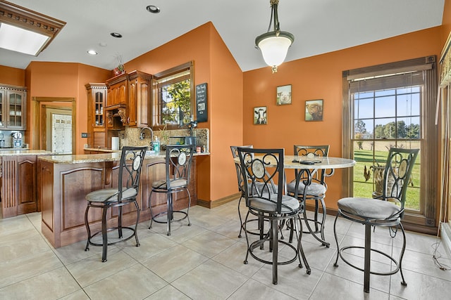 kitchen with light stone counters, brown cabinets, hanging light fixtures, decorative backsplash, and glass insert cabinets