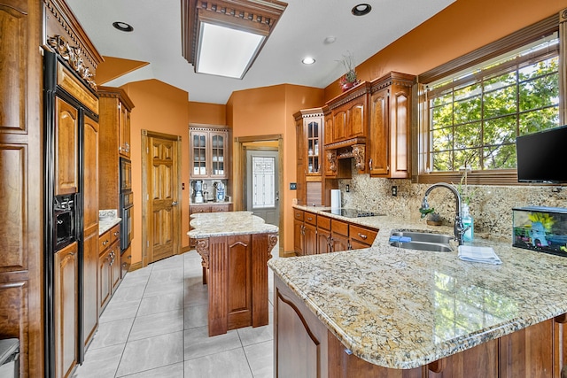 kitchen featuring glass insert cabinets, a kitchen island, a sink, light stone countertops, and black appliances