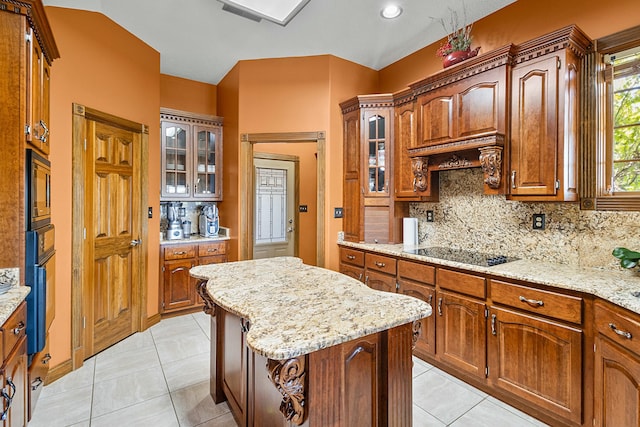 kitchen featuring a kitchen island, glass insert cabinets, black electric cooktop, and light stone counters